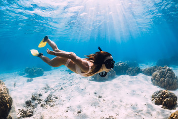 Freediver girl with fins glides over sandy bottom in blue ocean