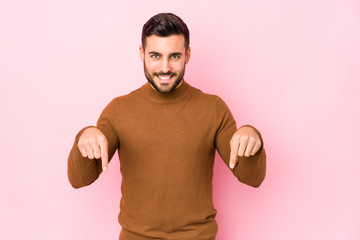 Young caucasian man against a pink background isolated points down with fingers, positive feeling.