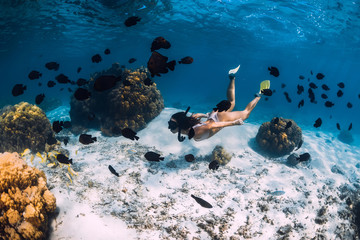 Naklejka na ściany i meble Freediver girl with fins glides over sandy bottom in blue ocean