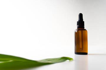 A small bottle with a dropper full of CBD oil or any other oil and a green leaf on white background