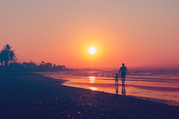 Man and kid silhouette going along sea shore on sun set backround, vacation evening. Parent and child, Father's day, Family with daughter, travelling with baby, girl, Holiday. Horizontal. Violet tone,