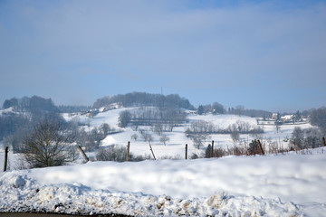 A field full of snow, in February 2015. There's some wooden barriers. On background, can see hills, covered by snow, with forest and several houses. It's in the french alps.