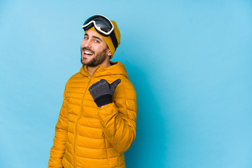 Young skier caucasian man isolated points with thumb finger away, laughing and carefree.