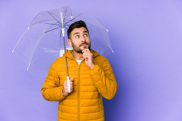 Young handsome man holding an umbrella isolated looking sideways with doubtful and skeptical expression.