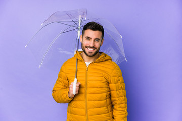 Young handsome man holding an umbrella isolated happy, smiling and cheerful.