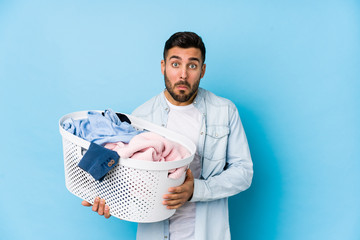 Young handsome man doing laundry isolated shrugs shoulders and open eyes confused.