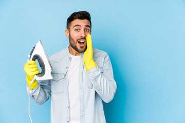 Portrait of young man ironing isolated is saying a secret hot braking news and looking aside