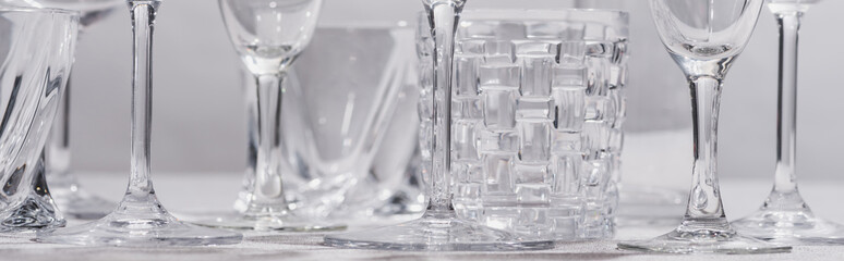 Panoramic shot of clear glasses on tablecloth on grey background