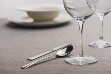 Selective focus of cutlery near clear wine glasses on tablecloth