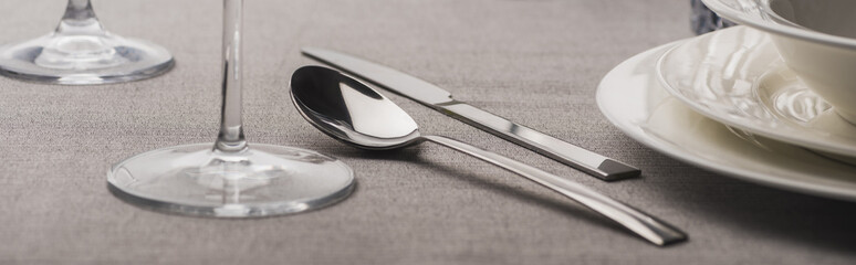 Spoon and fork beside wine glasses and plates on grey cloth , panoramic shot