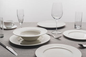 Dishware and transparent glasses on tablecloth on grey background