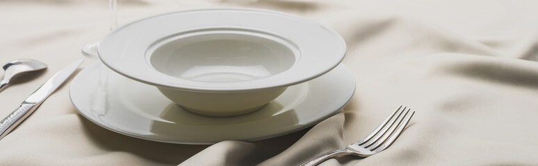 Panoramic shot of plates and cutlery on wavy white tablecloth