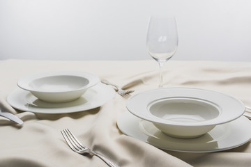 Selective focus of dinnerware and empty wine glass on tablecloth on grey background
