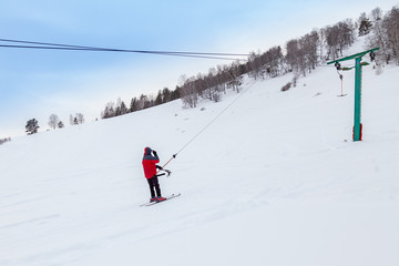 Fototapeta na wymiar A man skier climbs a mountain through the white snow clinging to a rope of a tow rope in a sports tourist base Turquoise Katun. Seasonal sports.