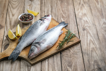 Fresh seabass and ingredients for cooking. Raw fish seabass with lemon, spices and herbs on wooden...