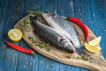 Fresh seabass and ingredients for cooking. Raw fish seabass with lemon, spices and herbs on blue wooden rustic table. Top view with copy space.