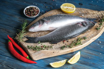 Fresh seabass and ingredients for cooking. Raw fish seabass with lemon, spices and herbs on blue wooden rustic table. Top view with copy space.