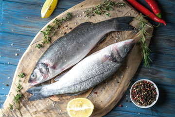 Fresh seabass and ingredients for cooking. Raw fish seabass with lemon, spices and herbs on blue wooden rustic table. Top view with copy space.
