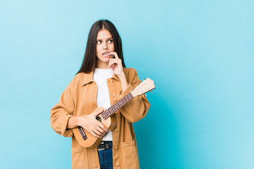 Young caucasian woman holding a ukelele relaxed thinking about something looking at a copy space.