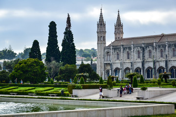 Obraz premium Lisbon, Portugal - 07.16.2019: Monastery of the Hieronymites (Mosteiro dos Jerónimos), a park near the building, green trees and bushes, tourists walk, in the summer afternoon.
