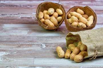 Peanuts lies in a coconut shell on a wooden table with place for text.