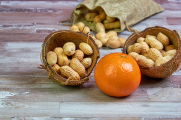 Peanuts lies in a coconut shell on a wooden table with orange tangerine fruit, healthy food, raw food