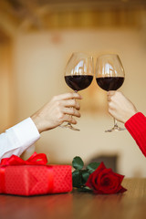 Hands holding glasses of wine on restaurant background. Couple clink glasses with red wine. Valentines day celebration concept. Relationship, surprise and love concept.