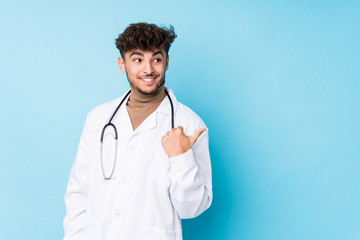 Young arab doctor man idolated points with thumb finger away, laughing and carefree.