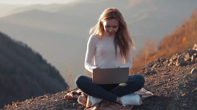 Wide shot of Female girl young women in white work on laptop computer with epic beautiful scenic view of mountains background. morning outdoors