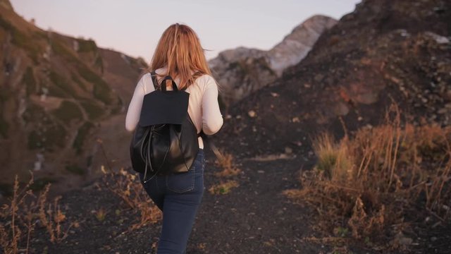 LIVE GIMBAL SHOT. Back view of young women attractive girl walking outdoors on background of mountain landscape , slow motion, close up. black backpack and white clothes