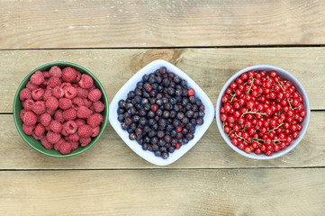 Bowls with fresh garden and forest berries: raspberry, purple shadberry, red currant overhead on the wooden table, flat lay, from above top viiew, closeup, copy empty space for your design
