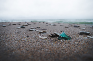 Low angle close-up of a piece of blue glass lying on a sandy seashore.
