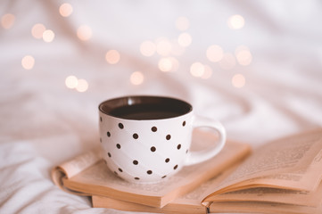 Morning cup of black tea with stack of open paper books in bed close up. Good morning. Breakfast.