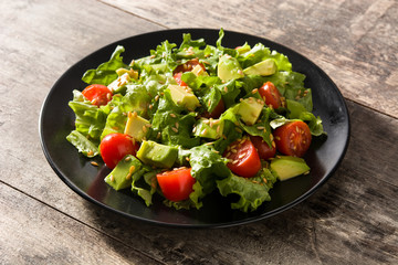 Salad with avocado, lettuce, tomato and flax seeds on wooden table