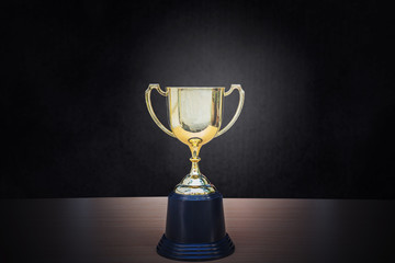 Golden trophy placed on top of old wooden table in front of dark background copy space ready for your design win concept.