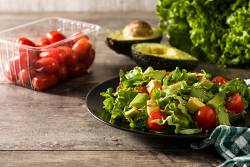 Salad with avocado, lettuce, tomato and flax seeds on wooden table. Copy space