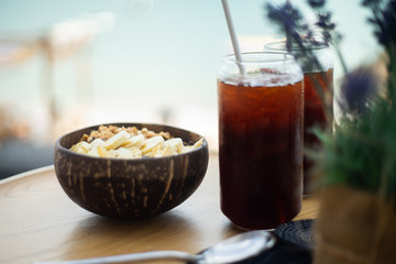 Maca root with cereal and banana split tropical vegetarian food in a bowl and black coffee in glass.