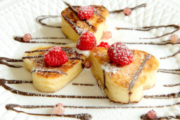 dessert three cheesecakes in the shape of hearts with berries watered with chocolate on a white plate on an isolated background