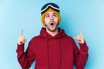 Young caucasian man wearing a ski clothes isolated pointing upside with opened mouth.
