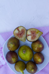 lots of ripe figs in a white plate on a white wooden background with a pink towel. the concept of healthy eating. vegan. live vitamins. cut figs. the view from the top. space for text