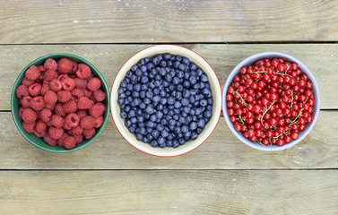 Bowls with fresh garden and forest berries: raspberry, blueberry, red currant overhead on the wooden table, flat lay, from above top viiew, closeup, copy empty space for your design