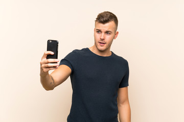 Young handsome blonde man over isolated background making a selfie