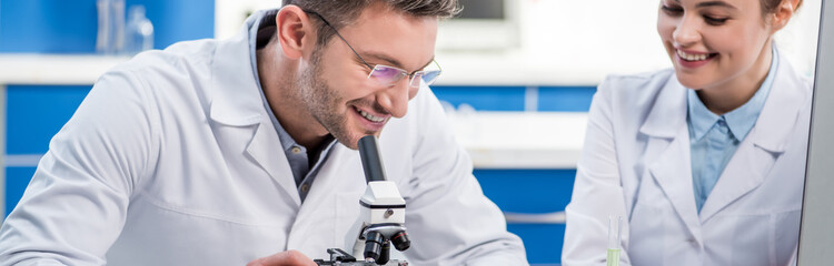 panoramic shot of smiling molecular nutritionists using microscope in lab