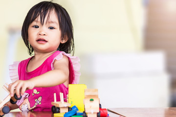 Portrait image of​ Asian baby​ girl​ playing​ the​ wooden​ block toys.​ On​ wooden​ table.​ 1-2​ years​ old​ of​ child.​ Learning​ and​ development​ of​ kid​ concept. With copy space.