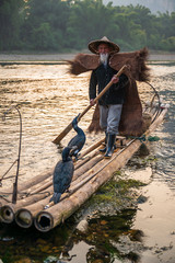 A fisherman and his cormorants on a raft in sunset