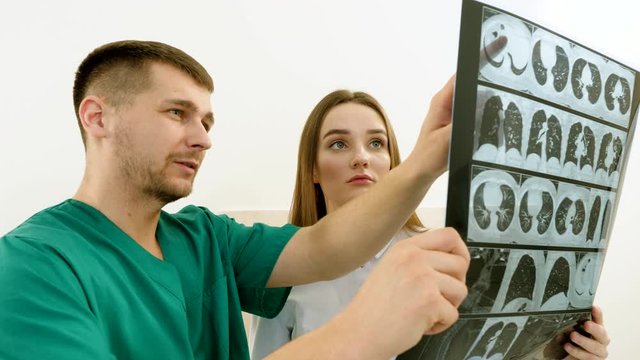 Closeup of two young doctors looking at an x-ray scan of lungs in modern clinic. 4K