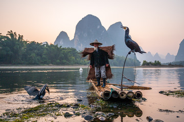 A fisherman and his cormorants on a raft in sunset