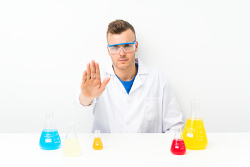 Young scientific with lots of laboratory flask making stop gesture with her hand