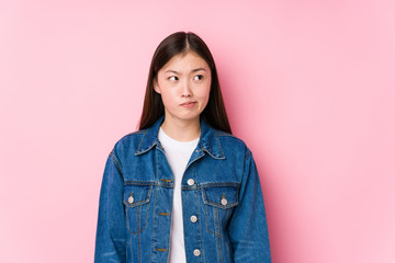 Young chinese woman posing in a pink background isolated confused, feels doubtful and unsure.