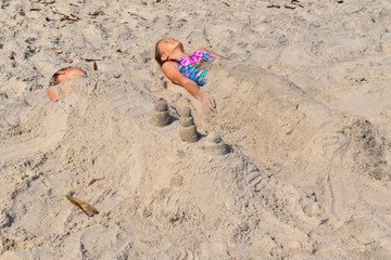 Fototapeta na wymiar Little girl lying on the sand. Children like mummies on the beach.